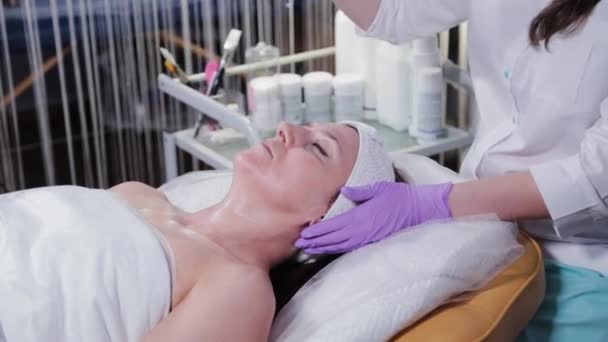 Kvinnlig kosmetolog applicerar peeling på kvinnor ansikte mot ansikte till klienten av cosmetology kliniken. — Stockvideo