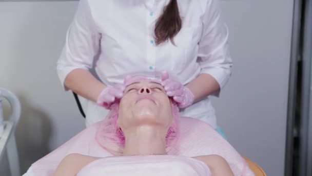 A kozmetikus nő krémet dörzsöl egy kozmetikai klinika ügyfelének arcára.. — Stock videók