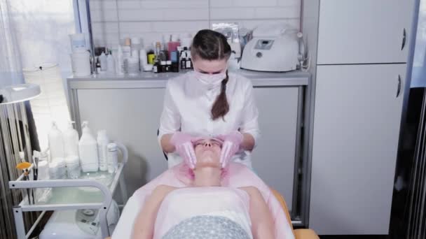 Kobieta kosmetyczka masuje kremem twarz klienta kliniki kosmetologicznej. — Wideo stockowe