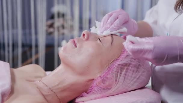Mujer esteticista lava la cara del cliente de la clínica de cosmetología. — Vídeos de Stock