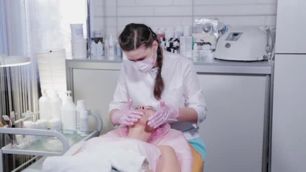 Kobieta kosmetyczka smaruje kremem twarz pacjentki. Masaż twarzy. — Wideo stockowe