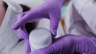 Kadın güzellik uzmanı bir kavanoz krema açar..