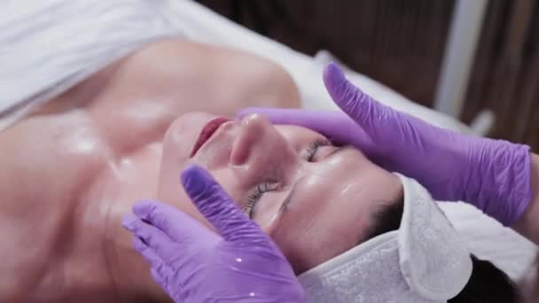 Femme cosmétologue massages femmes visage avec crème. — Video