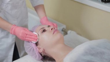 Kozmetologlar ellerinde pamuk pedlerle kaşlarını silerler. Güzellik uzmanı müşterilerine pamuk pedlerle kaşlarını ovar. Eldivenli güzellik uzmanı kıza kalıcı makyaj yapıyor. Kaş düzeltmesi..