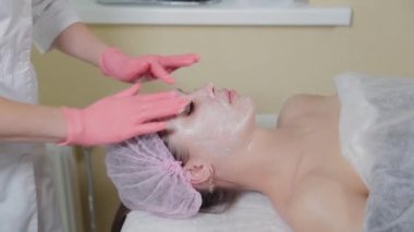 Profesyonel güzellik uzmanı yüzüne sıvı krem sürüyor..