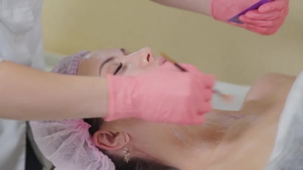Профессиональный косметолог наносит маску на лицо кистью на клиента. — стоковое видео