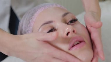 Profesyonel güzellik uzmanı bir kadının yüzüne sıvı sabun sürer..