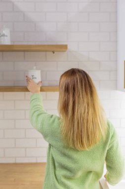 Mutfakta genç bir kadın raftan şeker alıyor..