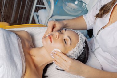Profesyonel güzellik uzmanı kadın müşteriye pamuk pedlerle yüzünü siliyor..
