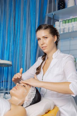 Profesyonel güzellik uzmanı bir kadına yüz masajı yapar..