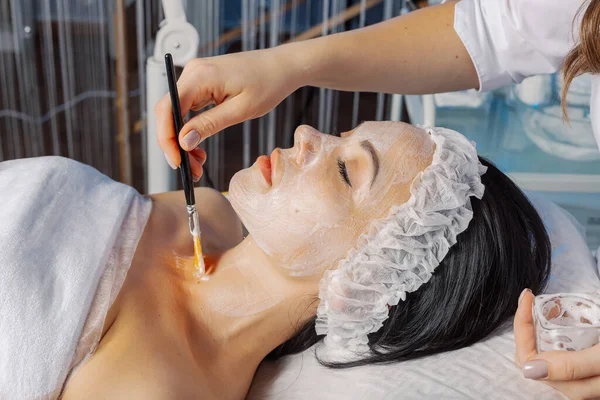 Professionelle Kosmetikerin trägt eine Maske mit einem Pinsel auf ihren Hals auf. — Stockfoto