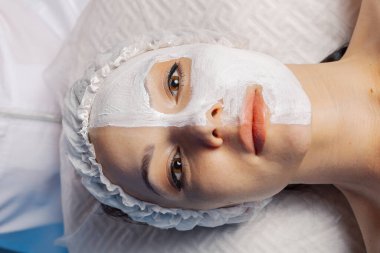 Yüzünde krem maske olan güzel genç bir kadın..