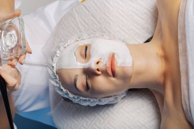 Yüzünde krem maske olan güzel genç bir kadın..