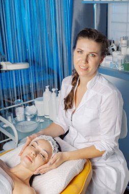 Profesyonel güzellik uzmanı bir kadına yüz masajı yapar..