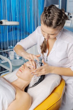 Profesyonel güzellik uzmanı bir kadına yüz masajı yapar..