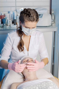 Profesyonel güzellik uzmanı bir kadına yüz masajı yapar..