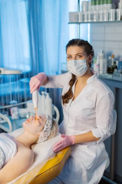 Yüzün Darsonvalizasyonu ya da elektroterapi yardımıyla yüzün gençleşmesi. Darsonval 'ın yüzü için bir fotoğraf. Şu anki terapi. Hasta güzellik uzmanında..