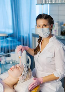 Yüzün Darsonvalizasyonu ya da elektroterapi yardımıyla yüzün gençleşmesi. Darsonval 'ın yüzü için bir fotoğraf. Şu anki terapi. Hasta güzellik uzmanında..