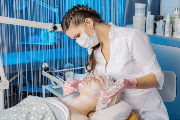 Mujer esteticista profesional aplica máscara con cepillo a la cara de los clientes. — Foto de Stock
