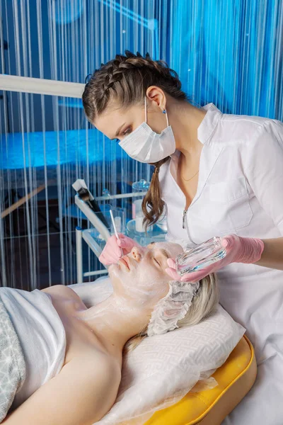 Mujer esteticista profesional aplica máscara con cepillo a la cara de los clientes. —  Fotos de Stock
