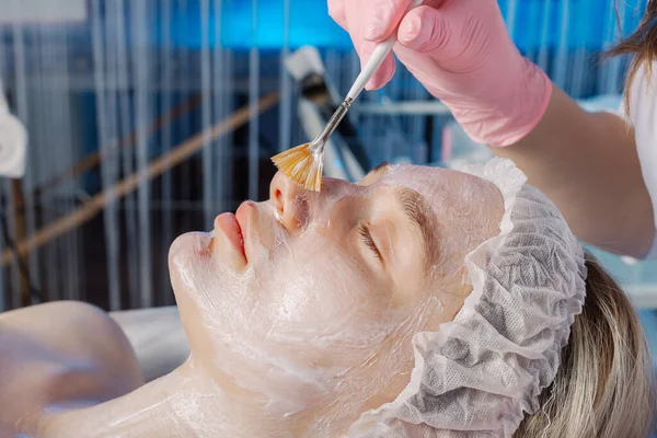 Professional beautician woman applies mask with brush to clients face. — Stock Photo, Image