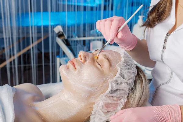 Professional beautician woman applies mask with brush to clients face. — Zdjęcie stockowe