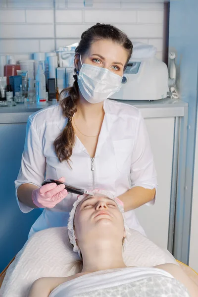 Un cosmetólogo profesional realiza un procedimiento de limpieza facial ultrasónica para una mujer. — Foto de Stock