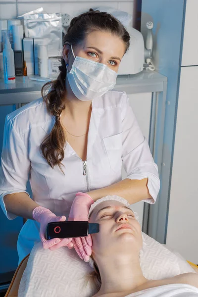 Un cosmetólogo profesional realiza un procedimiento de limpieza facial ultrasónica para una mujer. —  Fotos de Stock