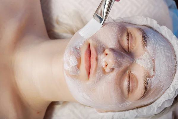 Professional beautician woman applies mask with brush to clients face. — Zdjęcie stockowe