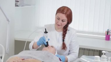 Profesyonel güzellik uzmanı kadın müşterisinin yüzüne karboksiterapi makinesi yapıyor..