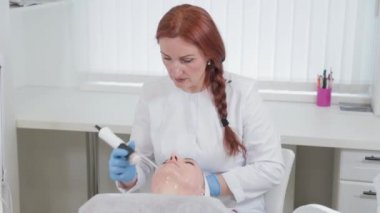 Profesyonel güzellik uzmanı kadın güzellik salonunda karboksiterapi cihazıyla yüz masajı yapıyor..