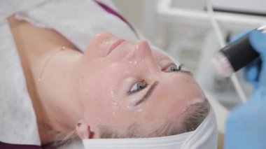 Profesyonel güzellik uzmanı kadın güzellik salonunda karboksiterapi cihazıyla yüz masajı yapıyor..