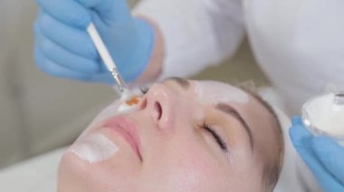 Profesyonel güzellik uzmanı kadın yüzüne fırçayla maske takıyor..