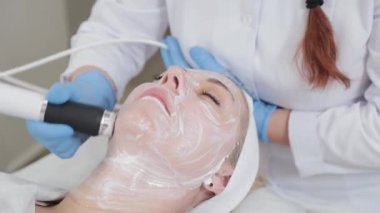 Profesyonel güzellik uzmanı kadın güzellik salonunda karboksiterapi cihazıyla yüz masajı yapıyor..