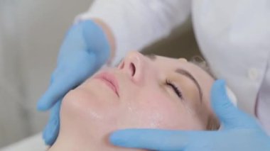 Profesyonel güzellik uzmanı yüzüne sıvı krem sürüyor..