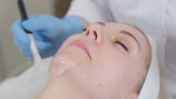 Esthéticienne professionnelle applique un masque sur le visage d'un client dans un salon de beauté. — Video