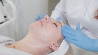 Profesyonel güzellik uzmanı kozmetoloji kliniğinde bir kadının yüzüne masaj yapıyor..