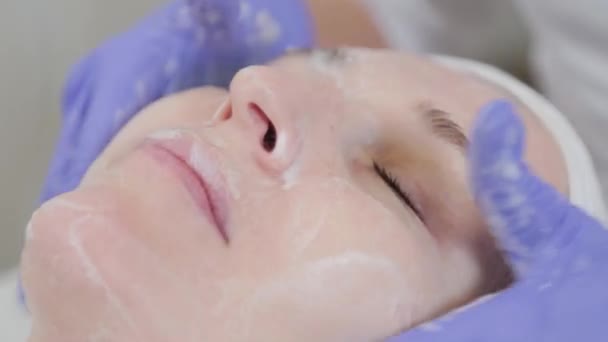 Professionelle Kosmetikerin reibt Flüssigseife auf das Gesicht einer Frau. — Stockvideo