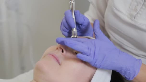 Woman beautician performs dermabrasion cosmetic procedure on clients face. — Stock Video