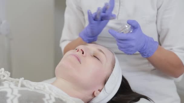 Kobieta kosmetyczka wciera krem nawilżający w twarz. — Wideo stockowe