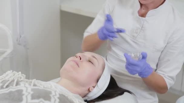 Mujer esteticista frota crema hidratante en su cara. — Vídeos de Stock