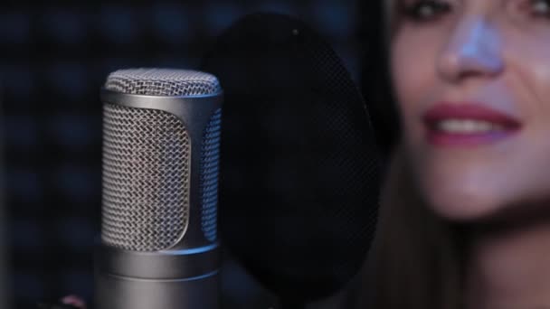 Happy beautiful young woman singing into microphone in recording studio. — Stock Video