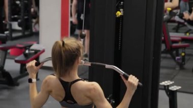 Güzel genç bir kadın spor salonundaki simülatörde sırtını çalıştırıyor..