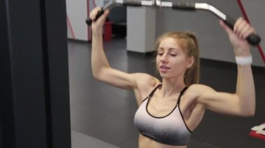 Güzel genç bir kadın spor salonundaki simülatörde sırtını çalıştırıyor..