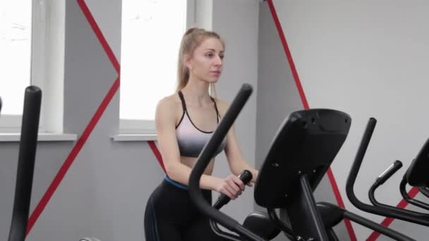 Frumos femeie tânără care lucrează pe un elipsoid în sala de gimnastică . — Videoclip de stoc