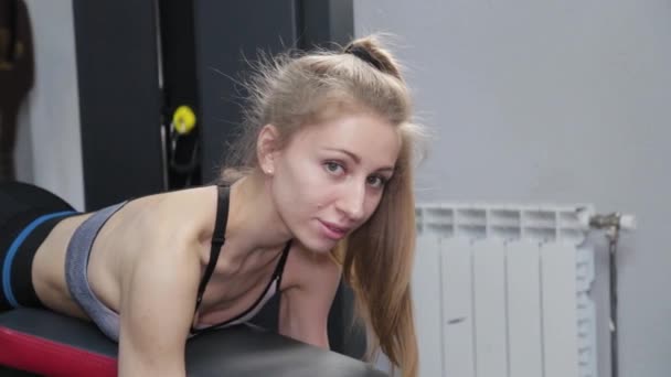 Hermosa mujer joven entrena piernas en el simulador en el gimnasio. — Vídeos de Stock