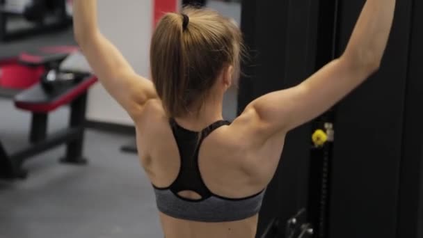 Vacker ung kvinna tränar ryggen på simulatorn i gymmet. — Stockvideo