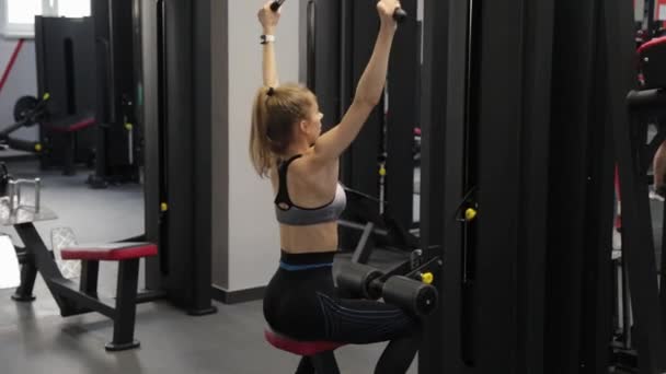 Schöne junge Frau trainiert ihren Rücken auf dem Simulator in der Turnhalle. — Stockvideo