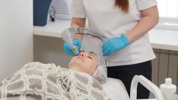 Mulher cosmetologista trata clientes rosto com laser. — Vídeo de Stock