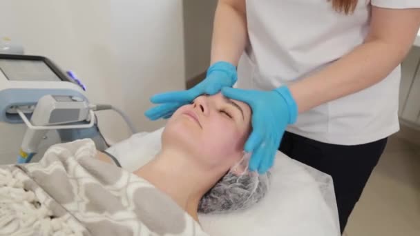 Mujer esteticista lubrica la cara de un cliente con crema. — Vídeos de Stock